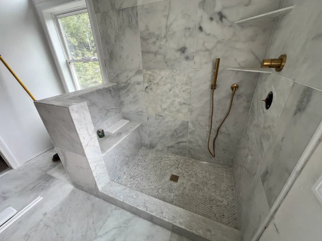Marble shower with bench and brass fixtures in a renovated Canton, MA bathroom