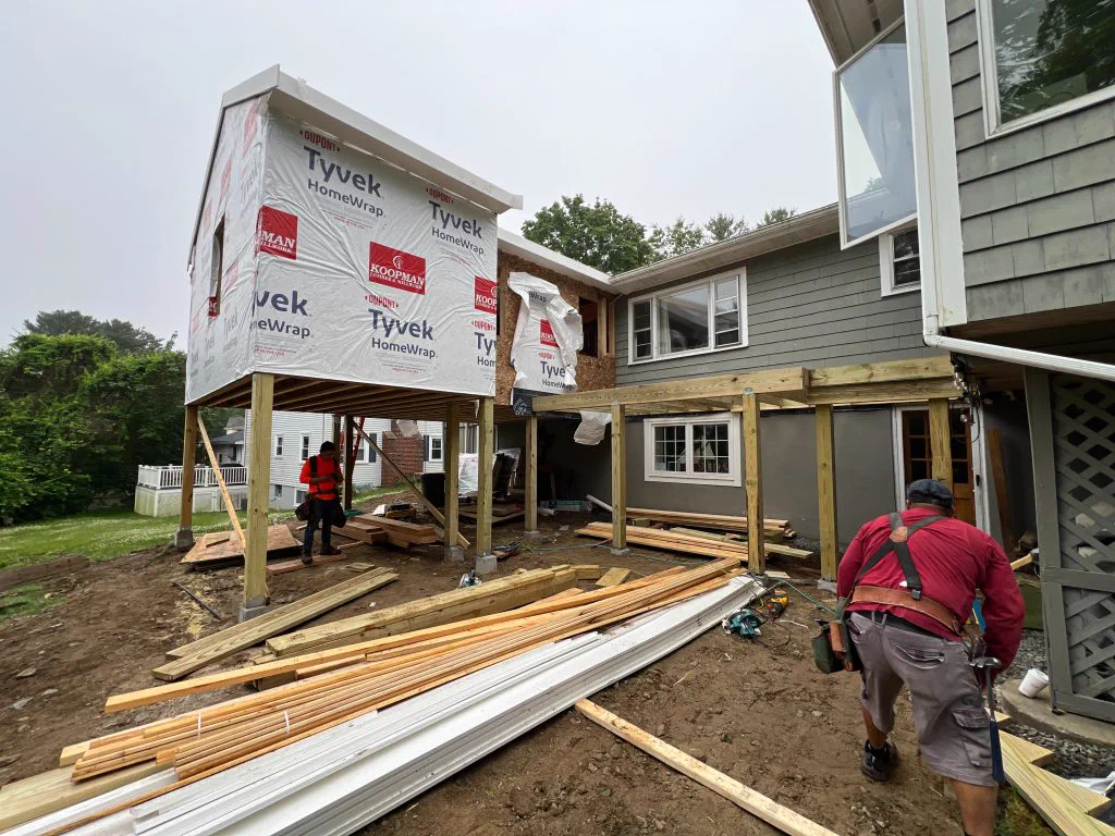 The addition framed, sheathed and wrapped on its columns, deck framing in place
