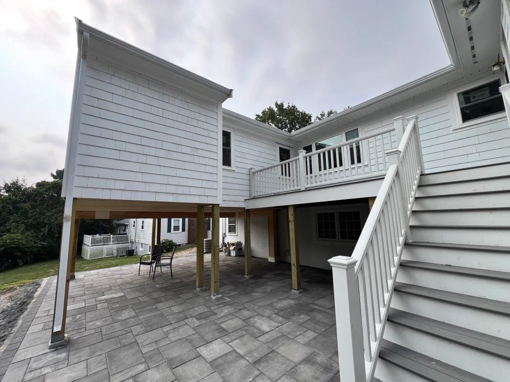 Finished white addition on columns with deck, stair and covered paver patio below