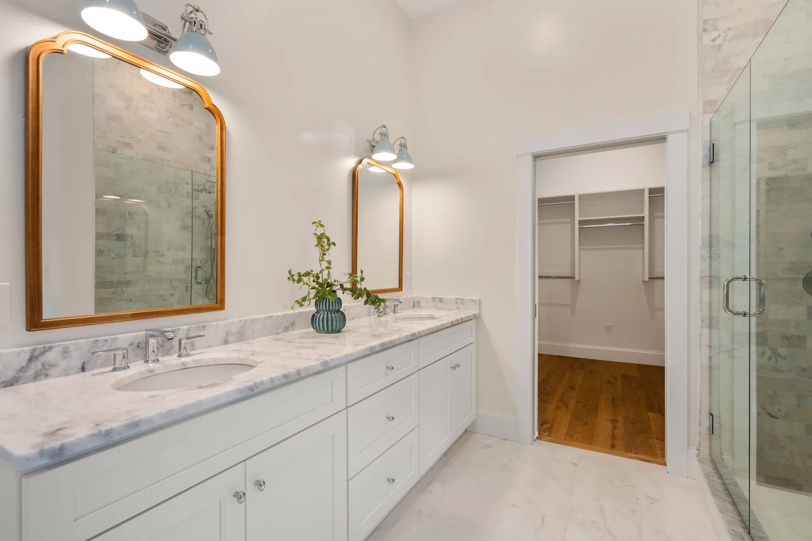 Marble primary bath with double vanity and arched gold mirrors