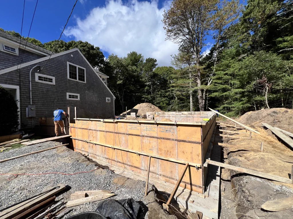 New foundation walls poured beside the existing shingled Cape in Osterville