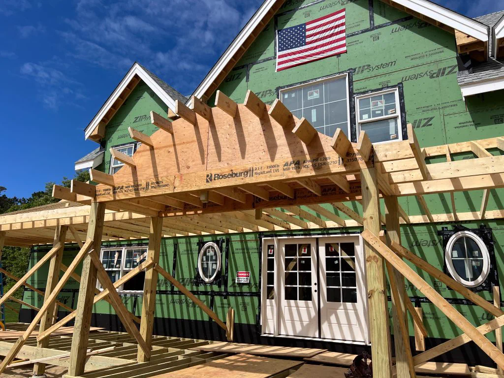 Curved porch roof framing on the shingle-style home, sheathed and ready to close in